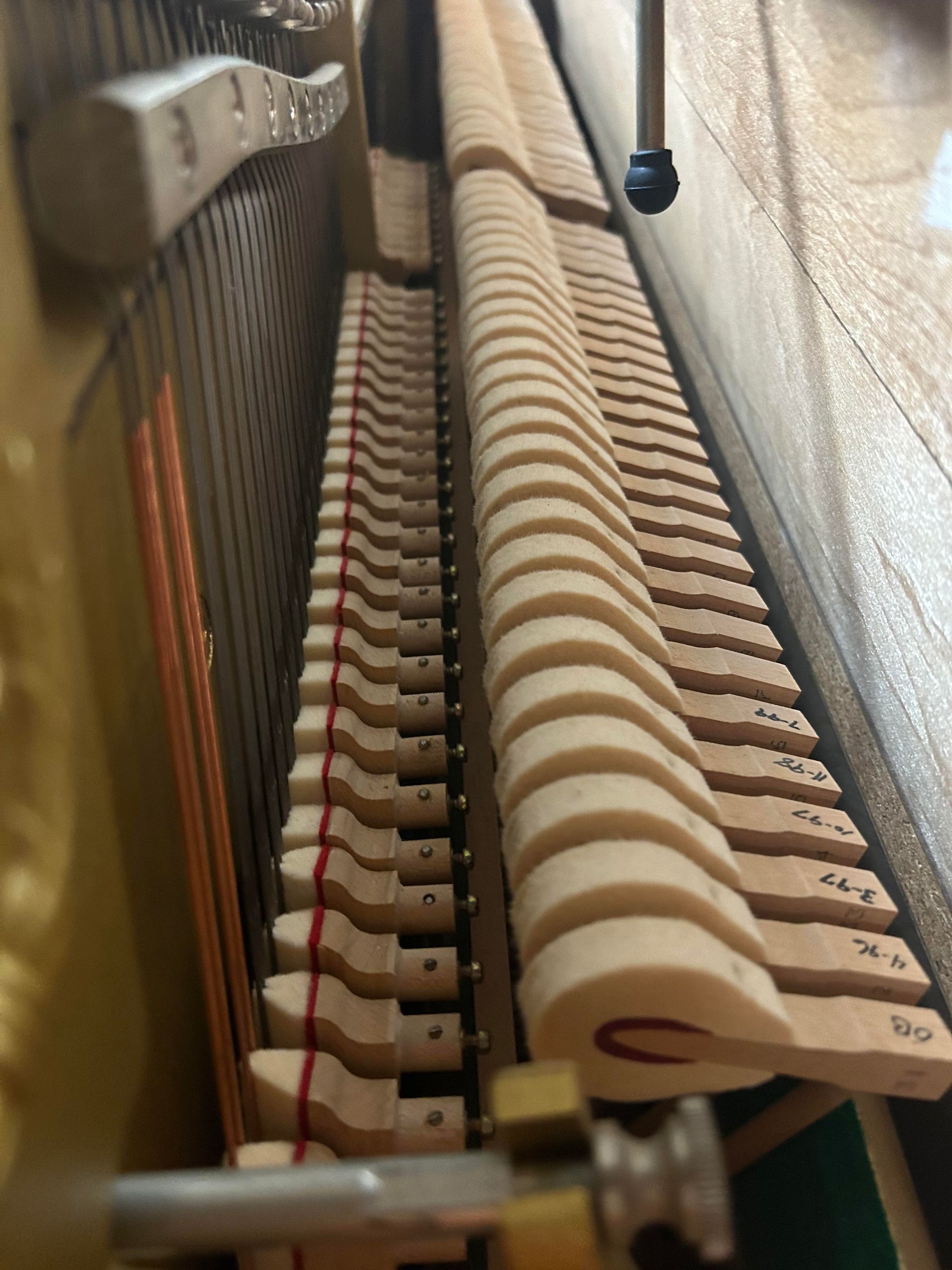 Piano's internal mechanism with hammers and strings visible. Wooden components, beige, brown, and metal parts.
