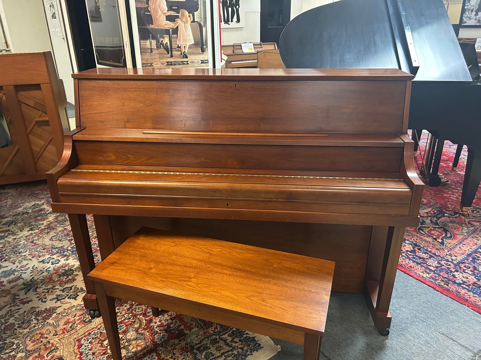 Wooden upright piano with matching bench in a showroom setting.