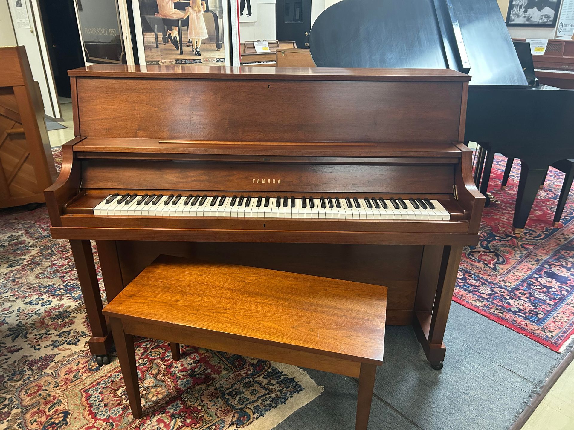 A wooden Yamaha upright piano with matching bench, indoors.