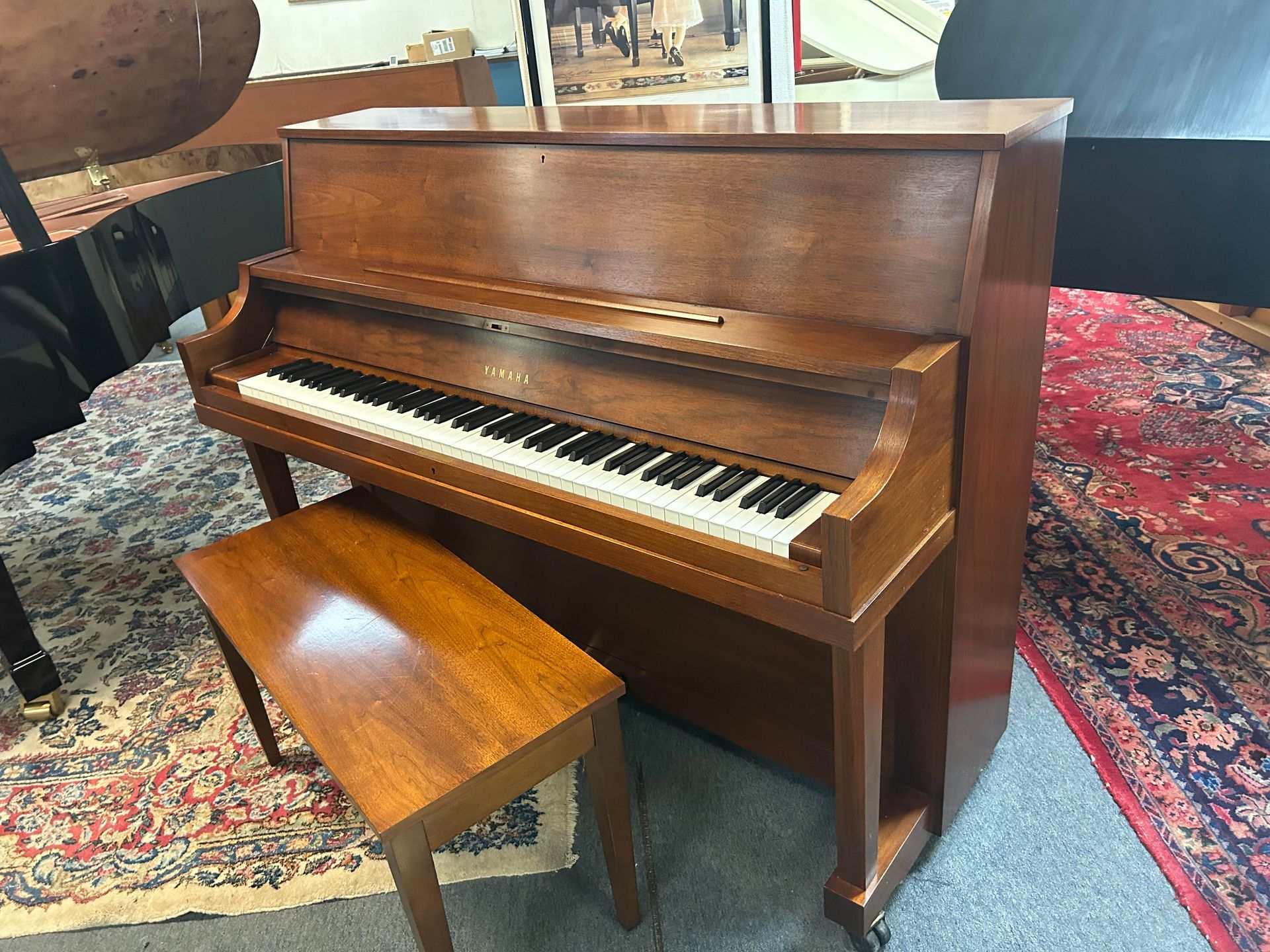 Brown upright piano with matching bench on a patterned rug.