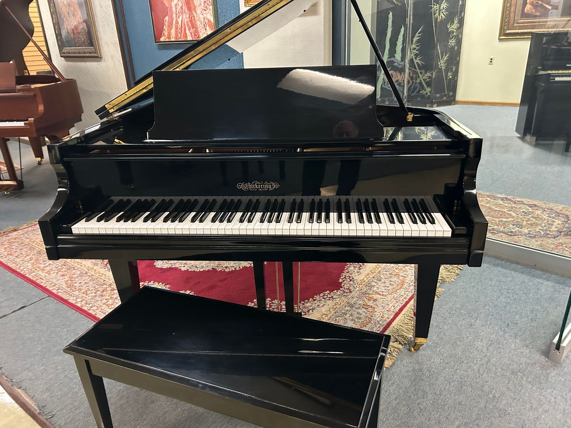 Black grand piano with open lid and matching bench in a showroom.