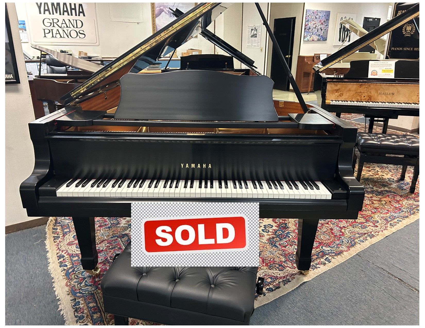 Black Yamaha grand piano with bench. Shop interior with piano and other pianos.