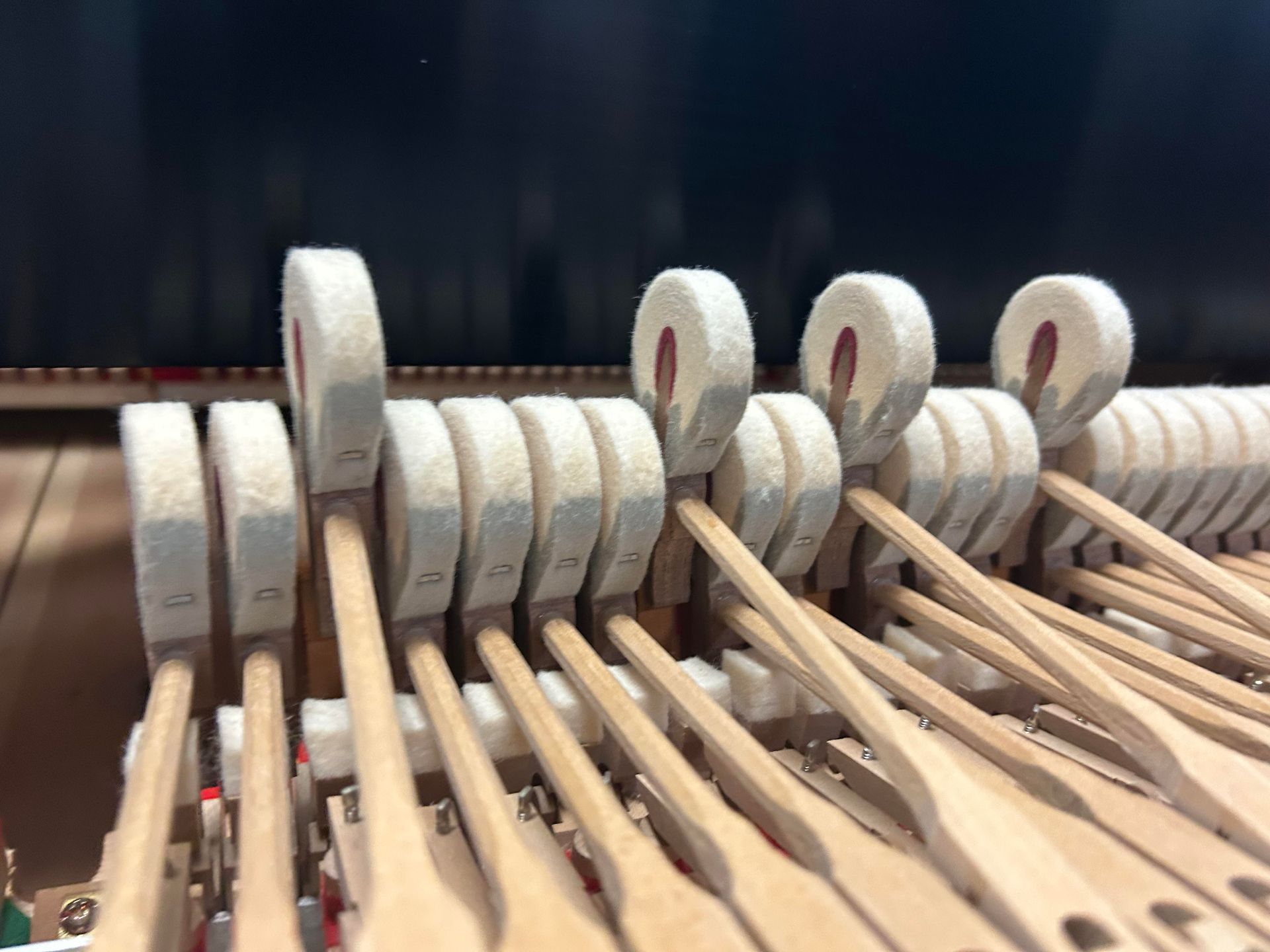 Close-up view of piano hammers, showing felt-covered striking surfaces, wooden shafts, and internal mechanisms.
