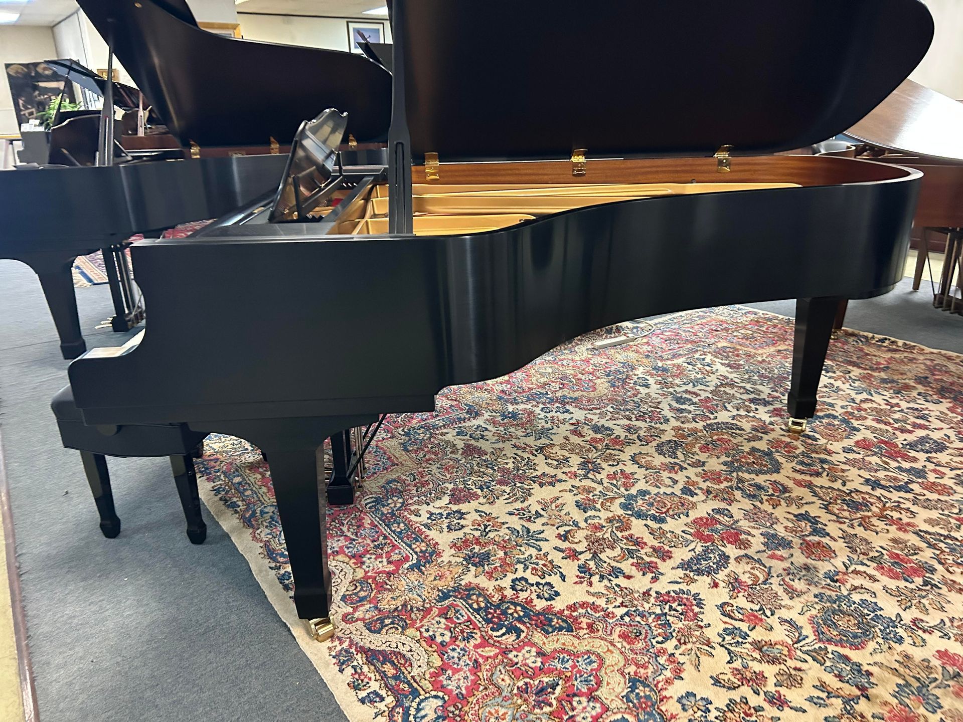 A black grand piano with its lid open, resting on a patterned rug.