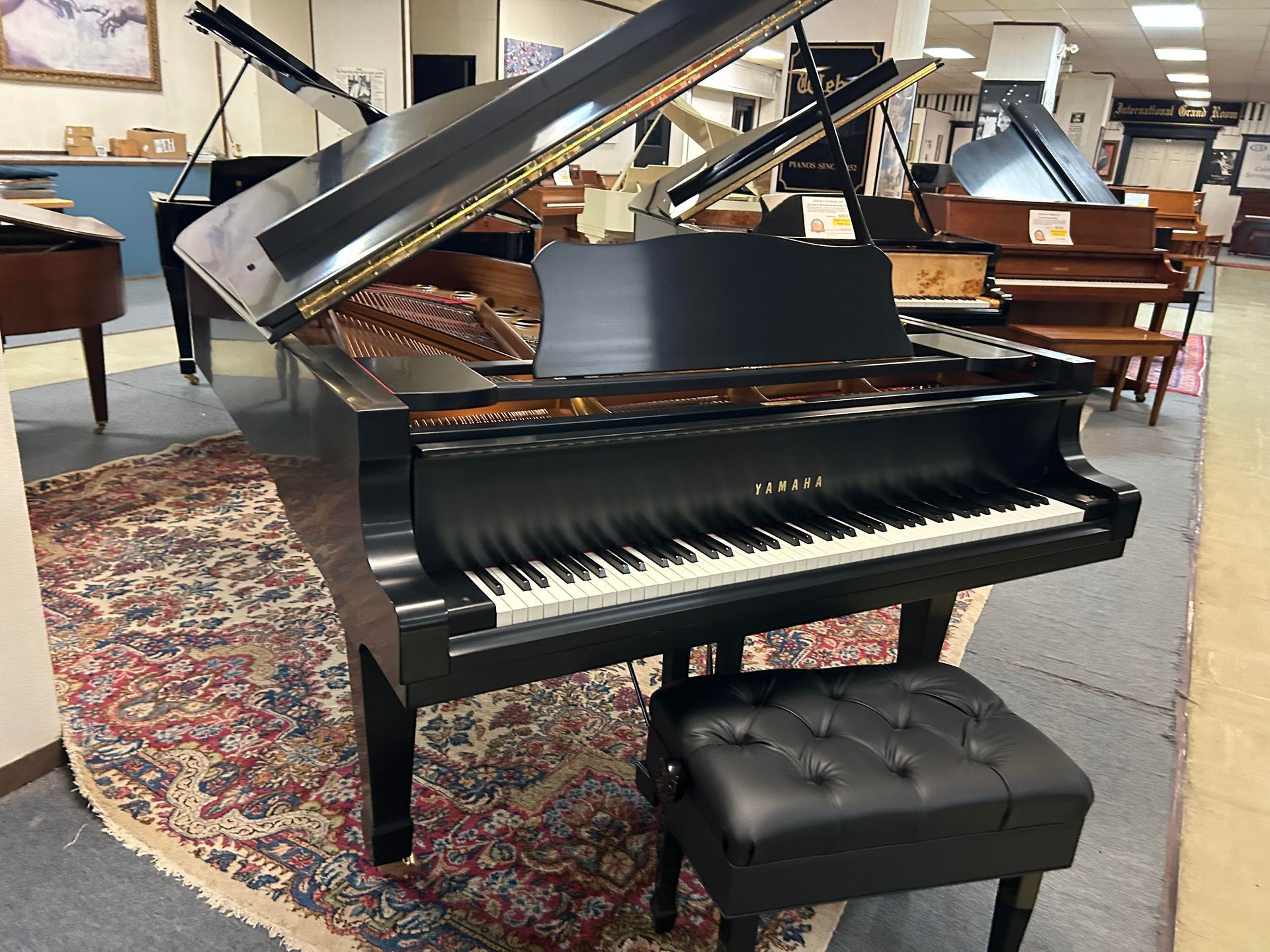 Black Yamaha grand piano with open lid and black stool on patterned rug.