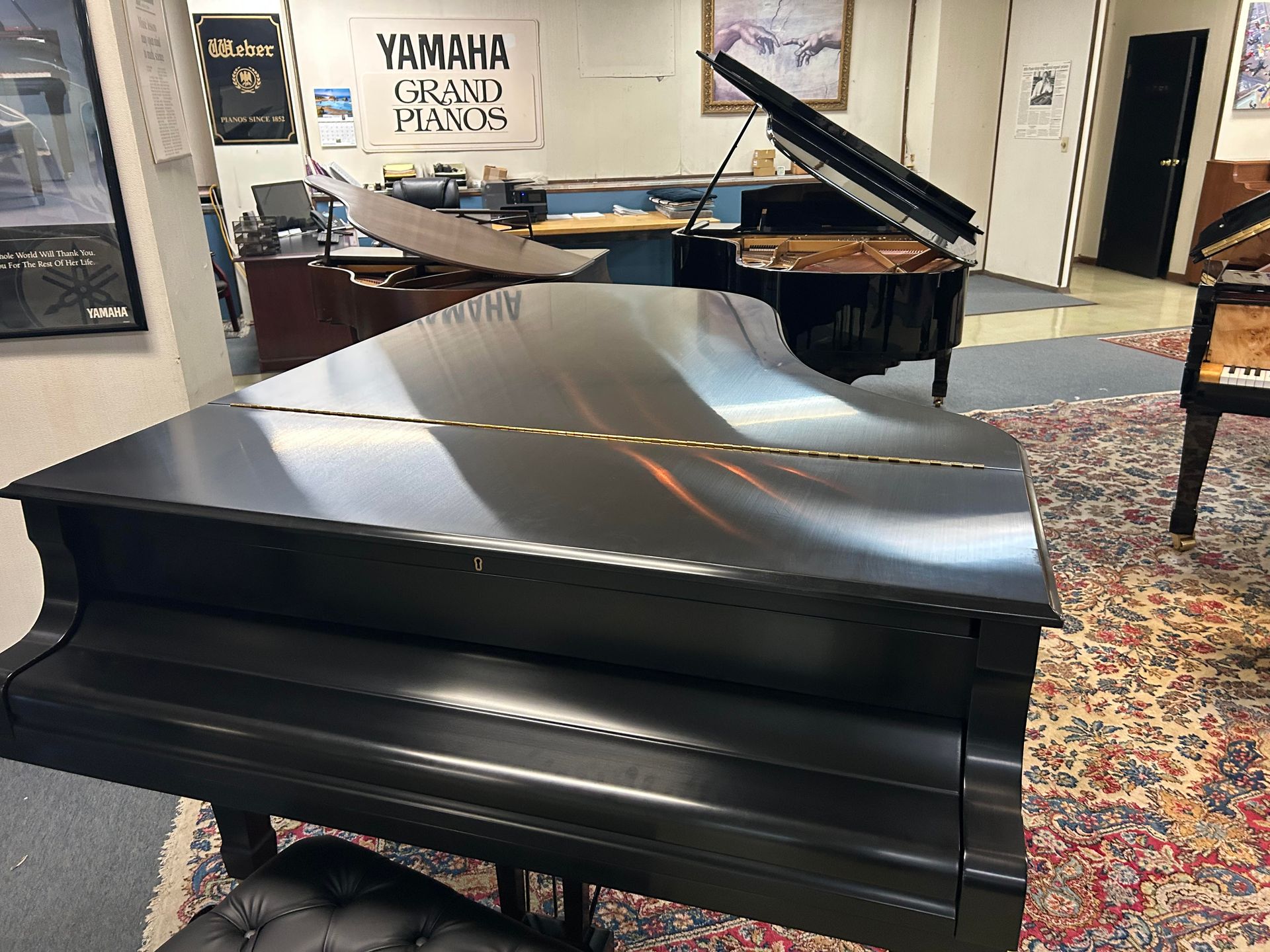 Black grand pianos in a music store, with a desk and office in the background.