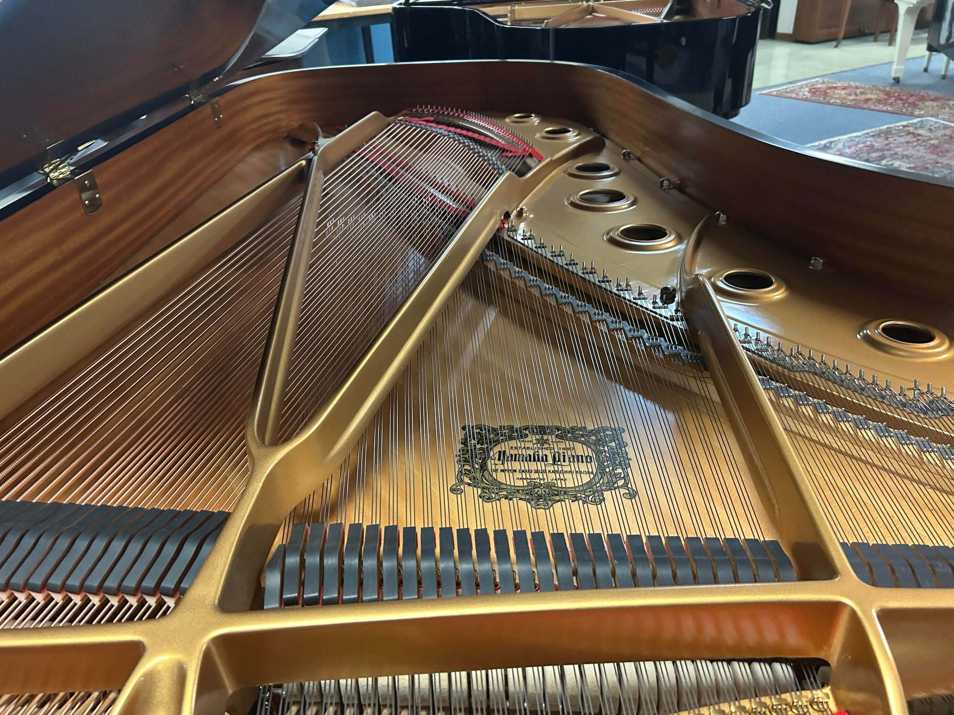 Interior of a grand piano, showing strings, soundboard, and structural components in a workshop.