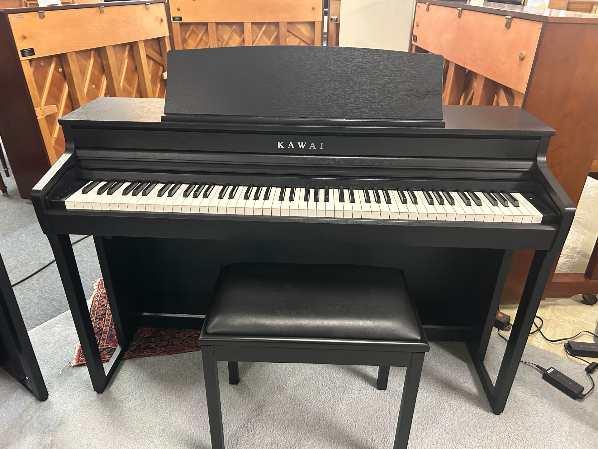 Black Kawai digital piano with matching bench in a room.