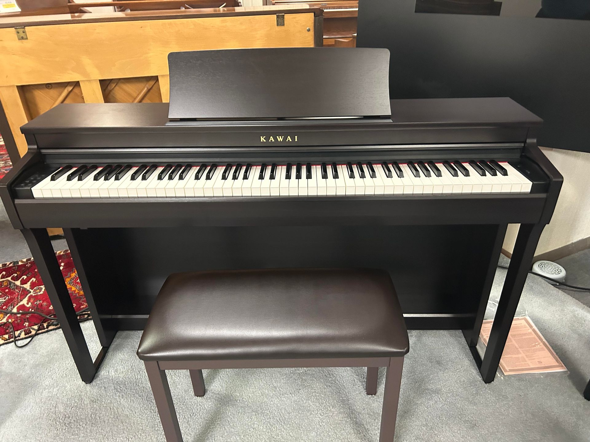 A dark brown Kawai digital piano with a matching bench. The music stand is up.