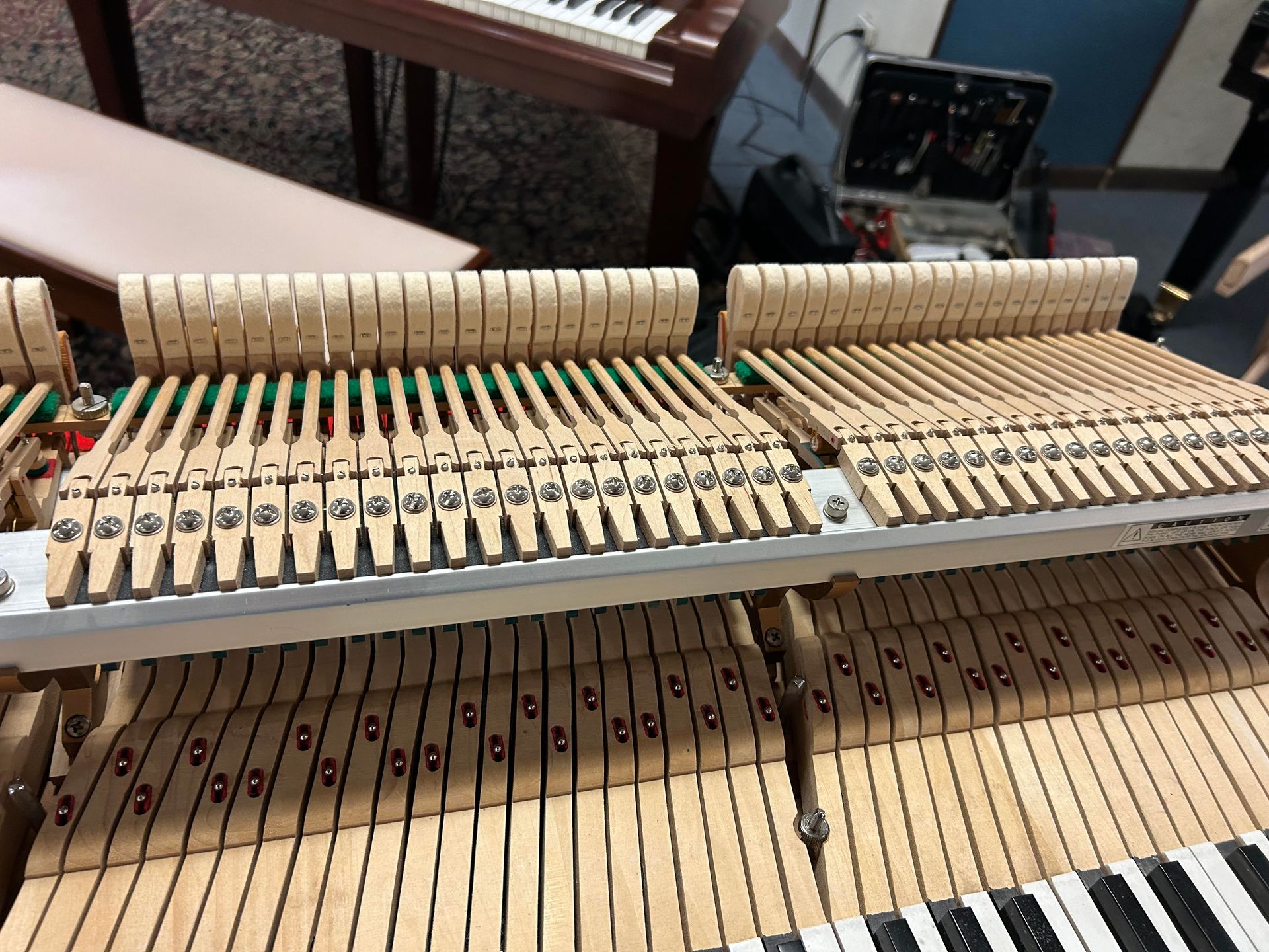 A close up of the inside of a piano with a keyboard in the background.
