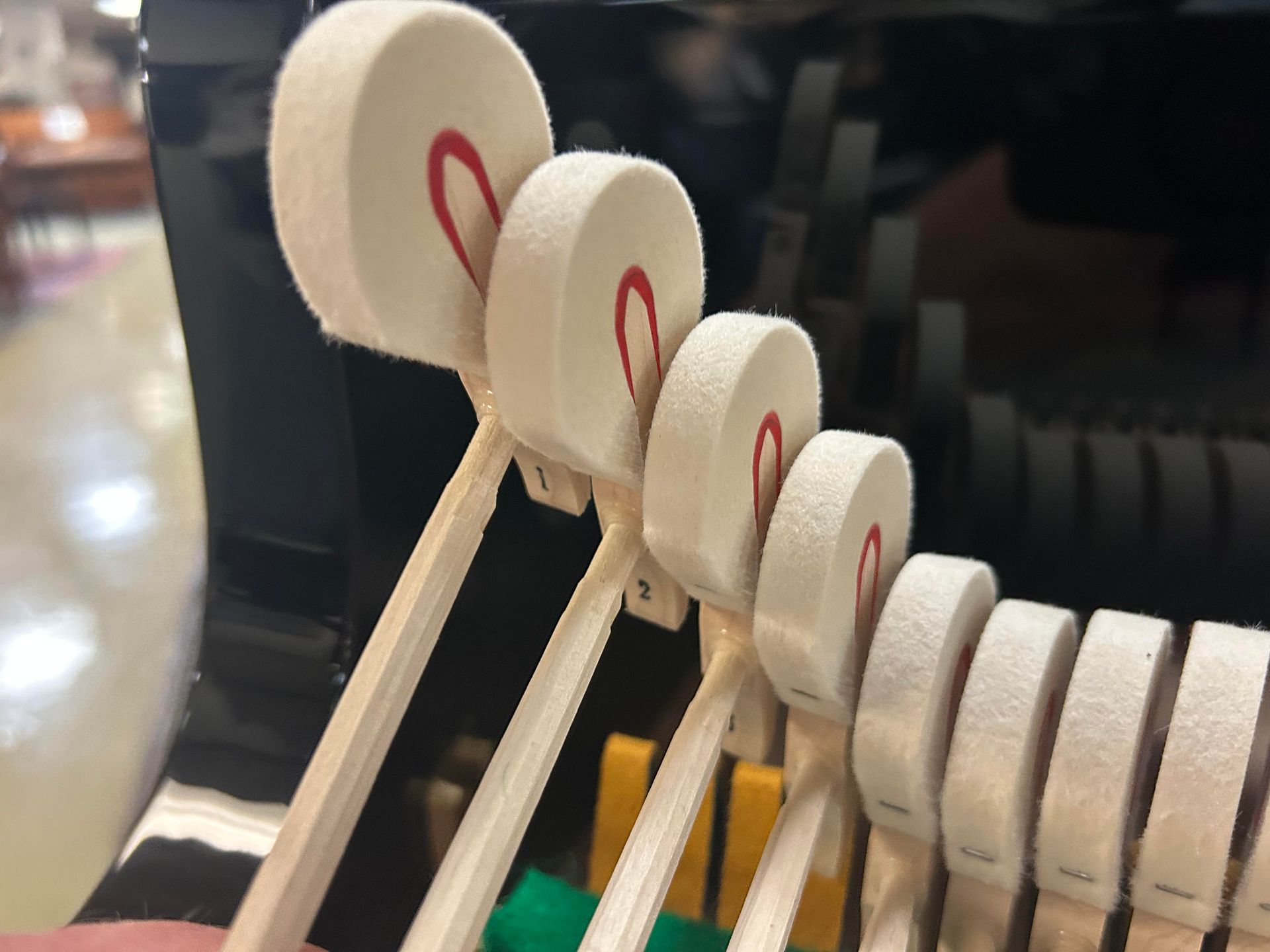 Piano hammers, white felt heads striking strings. Red felt accents. Black interior.