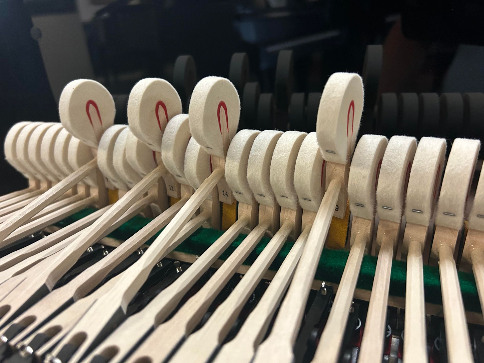 Close-up of piano hammers striking strings. Wooden levers with felt heads, red felt accents.