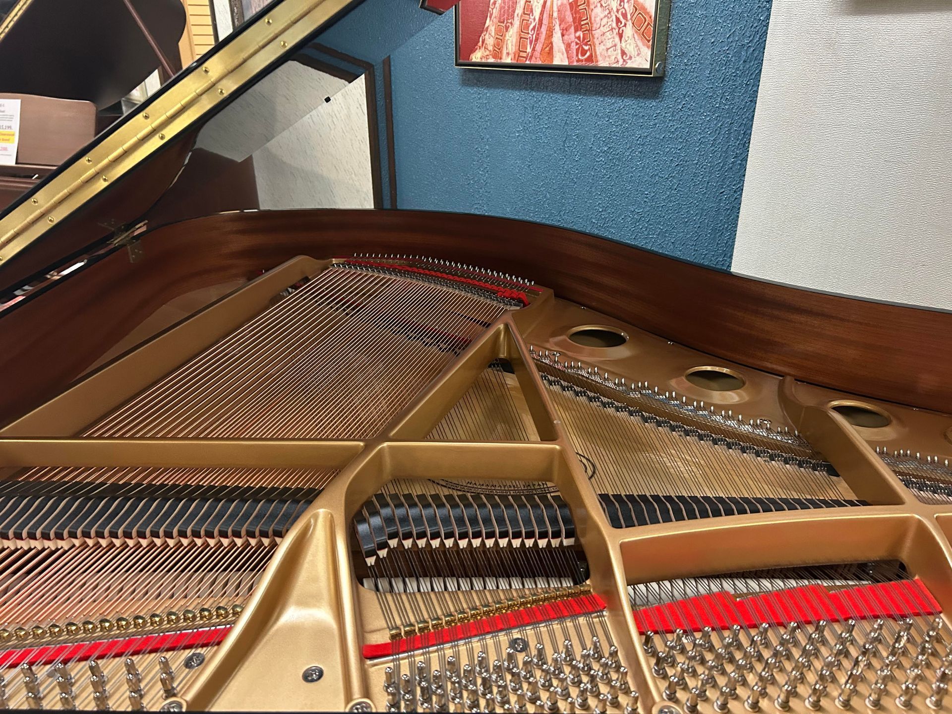 Inside of a grand piano, strings and internal mechanisms visible. Gold and wood tones contrast with blue wall.