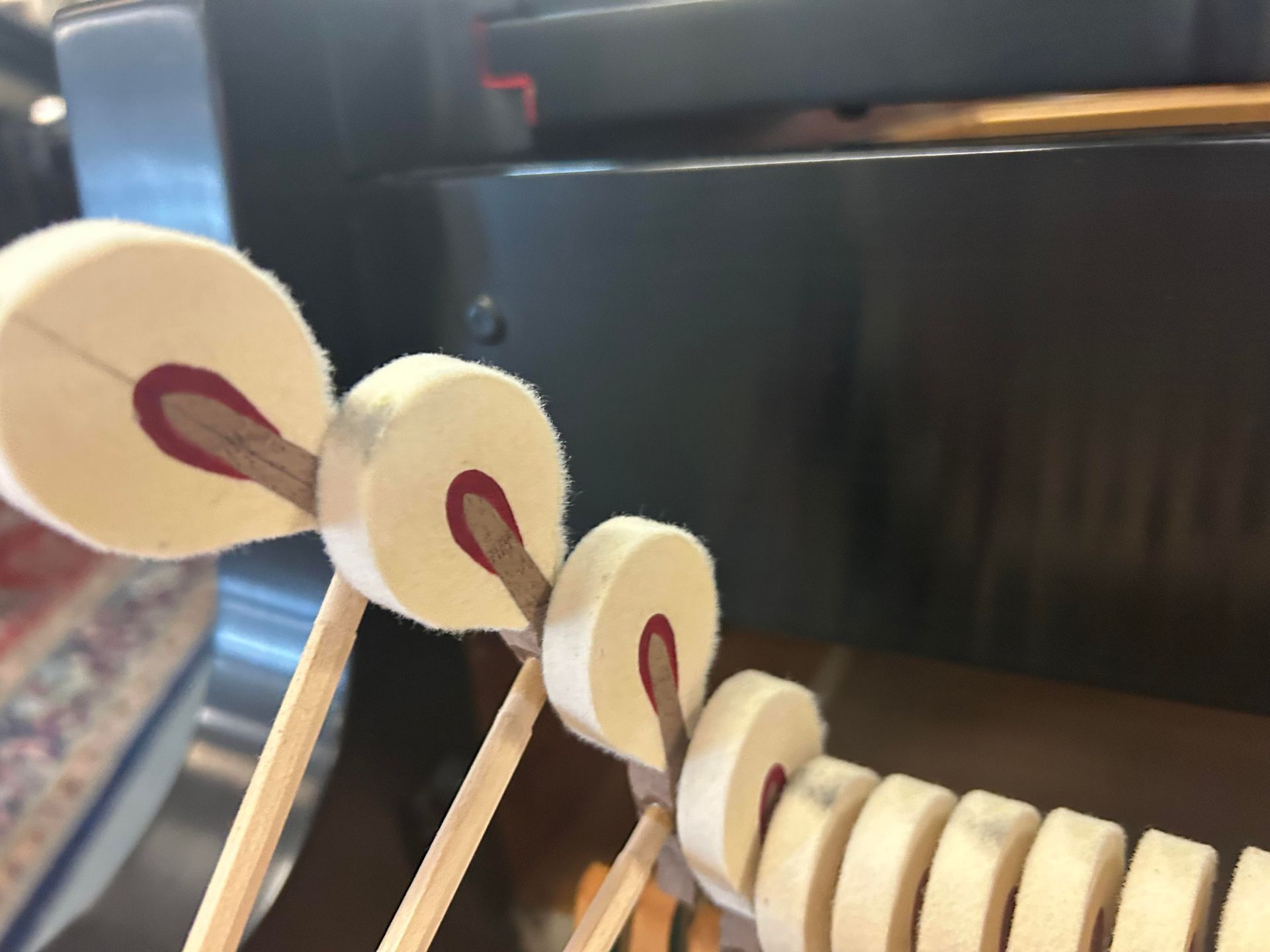 Piano hammers. Close-up view of the mechanism with felt heads striking strings. Wooden rods and dark frame.