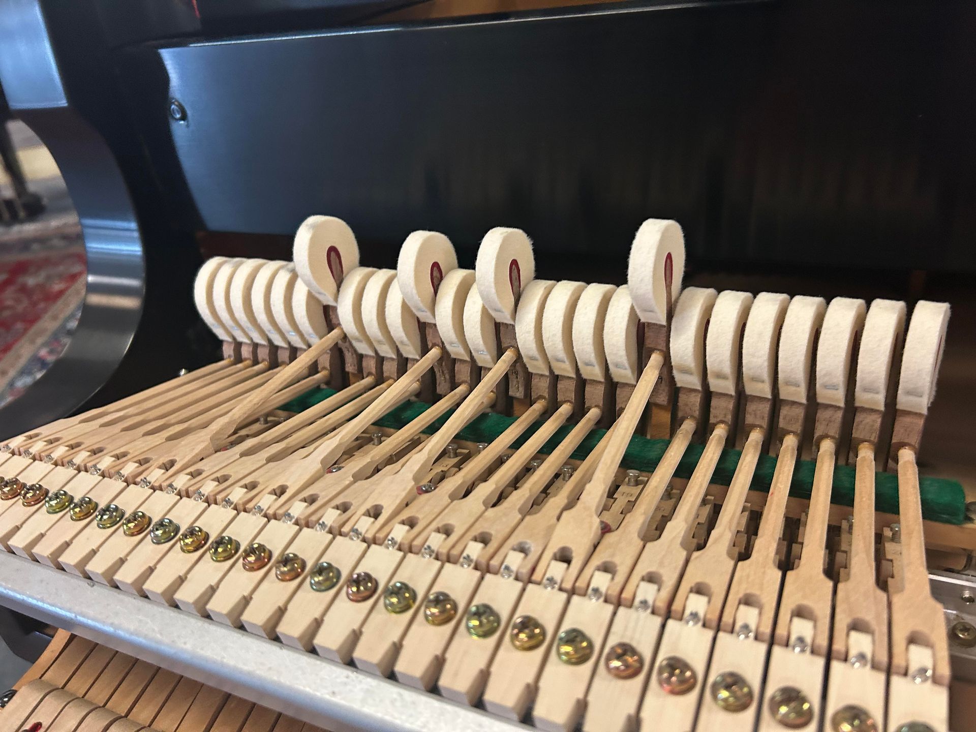 Piano hammers, felt-covered, striking strings. Wooden levers with brass screws are visible in close-up detail.