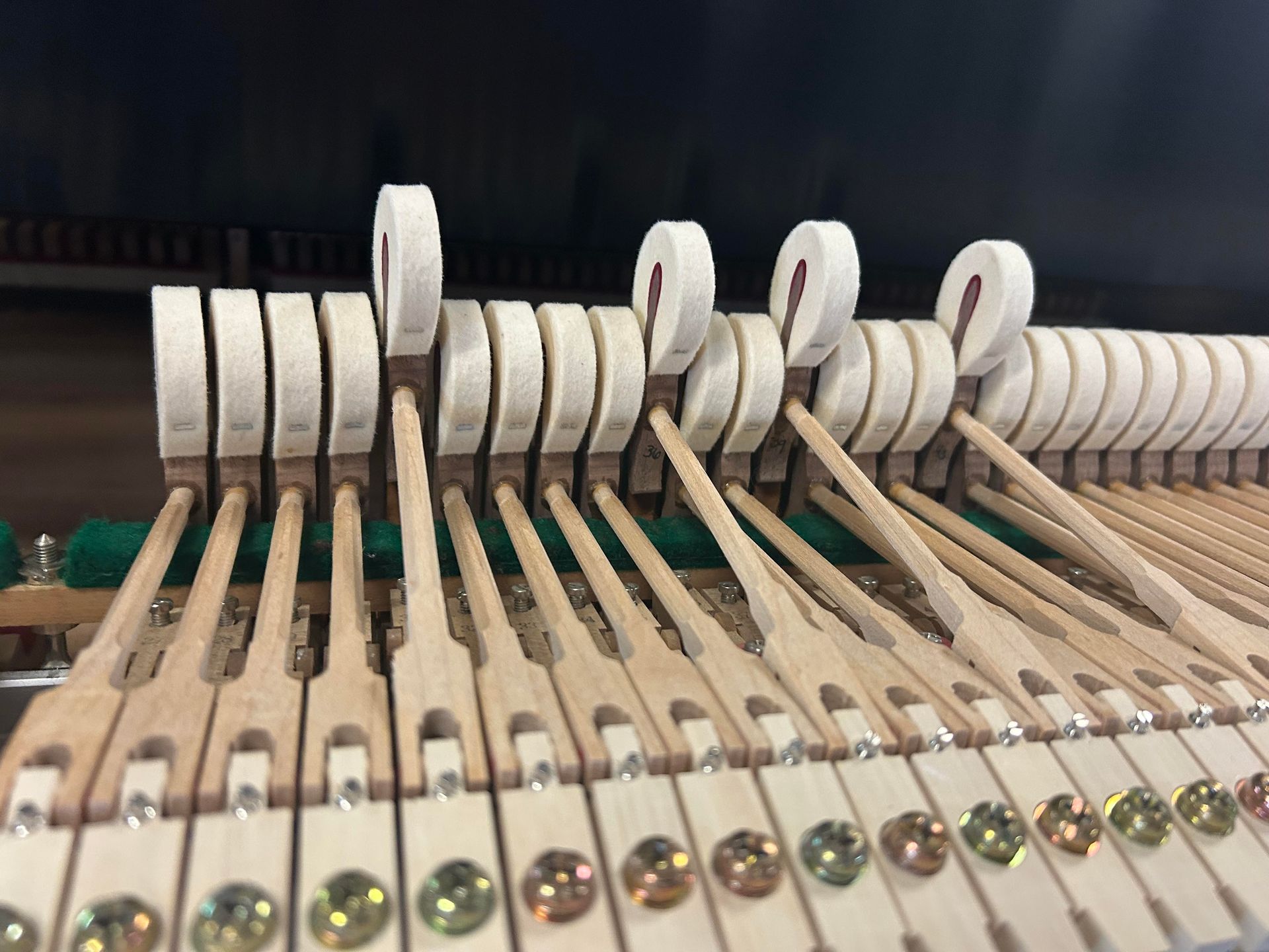 Close-up of piano hammers and action mechanism, showing wooden levers, felt pads, and metal screws.