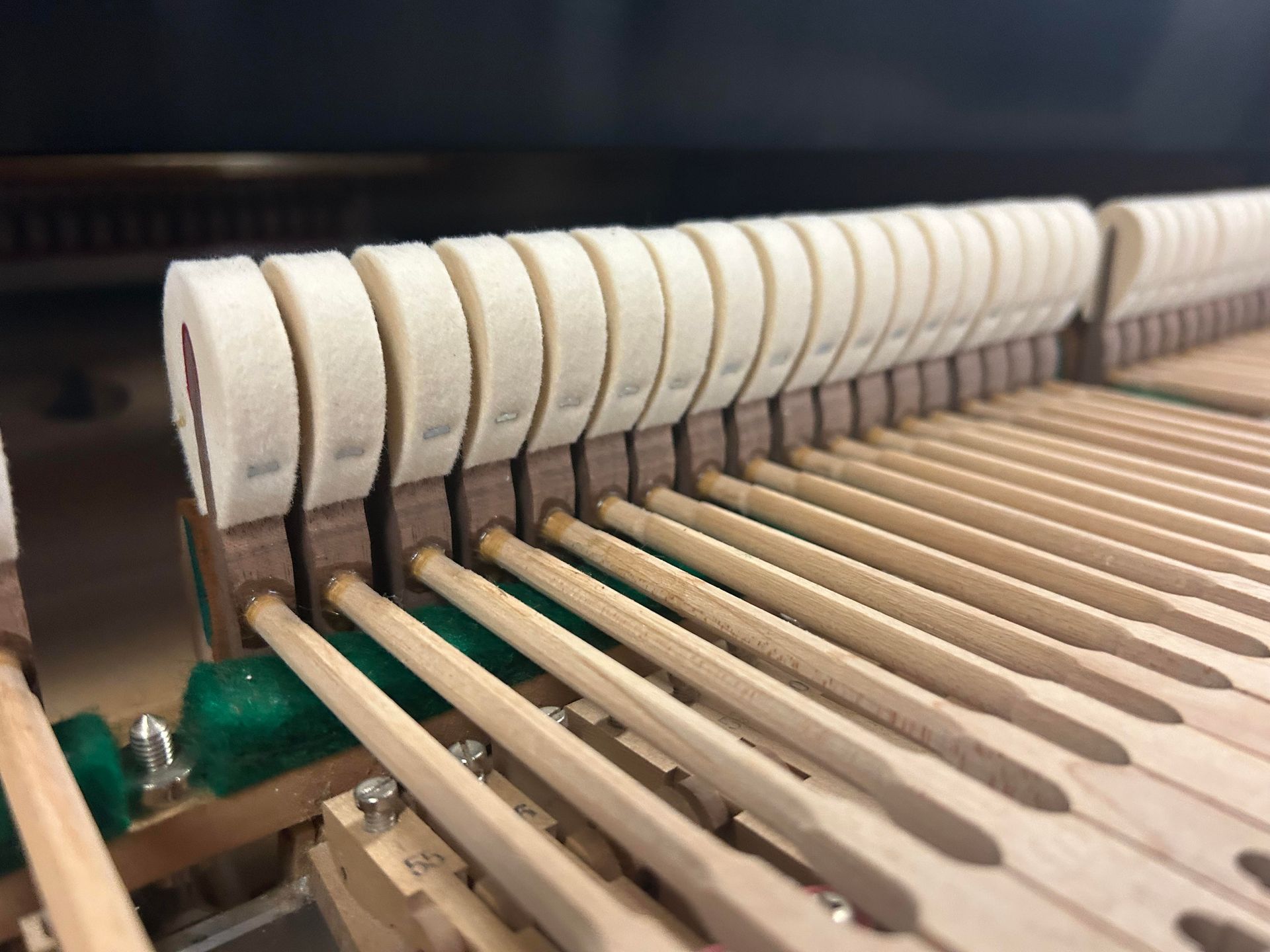 Piano hammers and action mechanism, close-up view. Wooden levers, felt-covered hammers, and metal hardware.