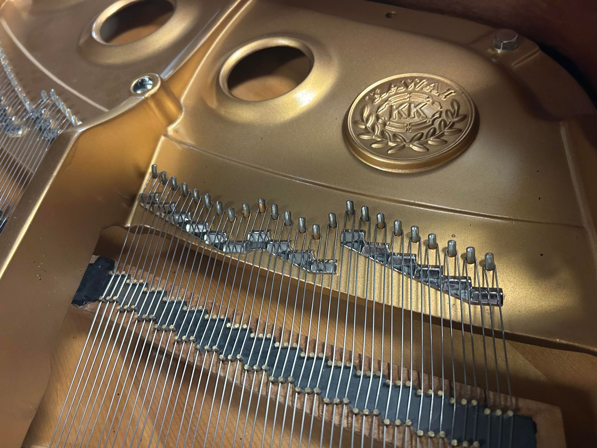 Gold-colored piano interior with strings, tuning pins, and a decorative emblem.