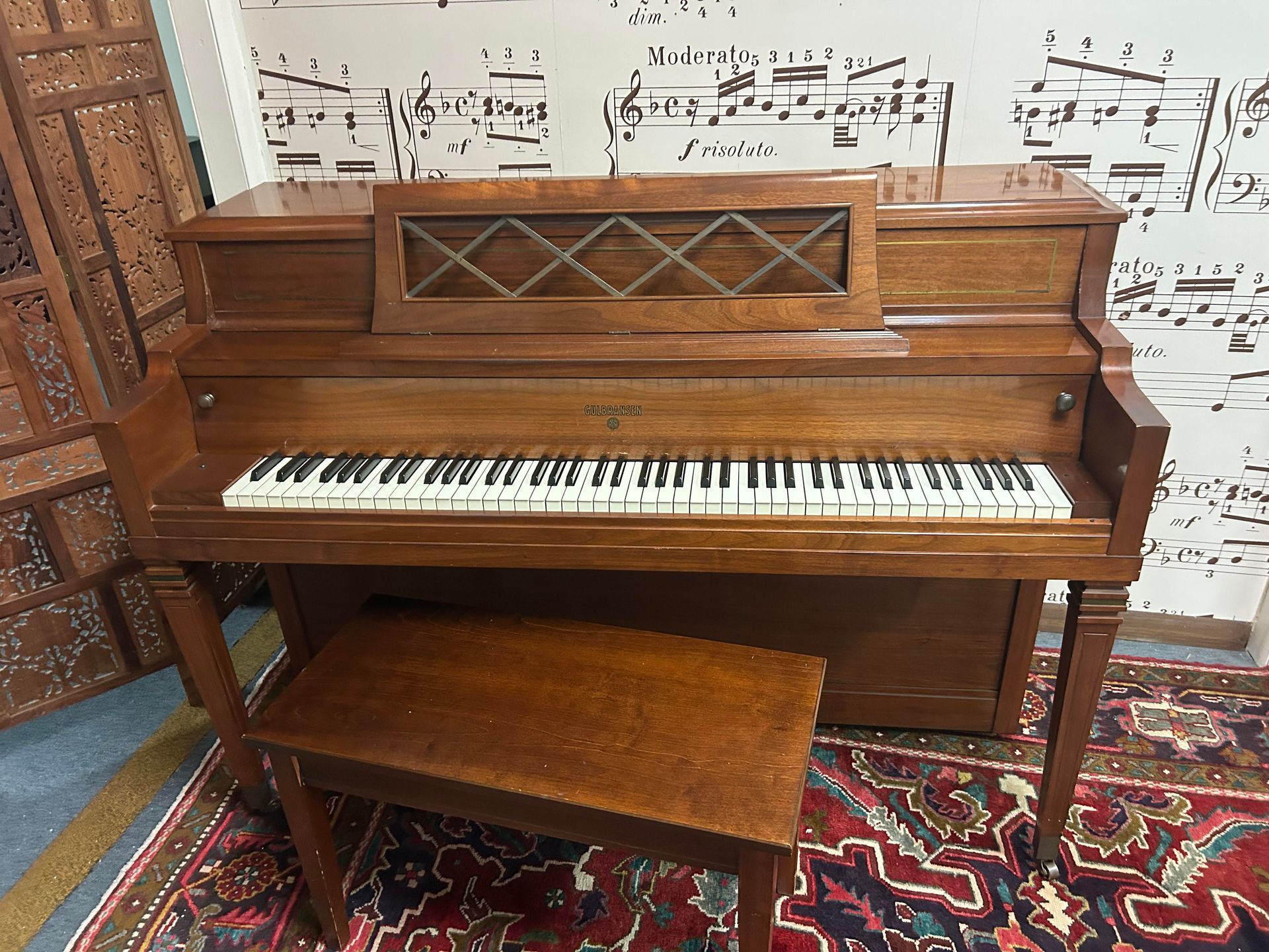 A piano with a bench in front of a wall with sheet music on it