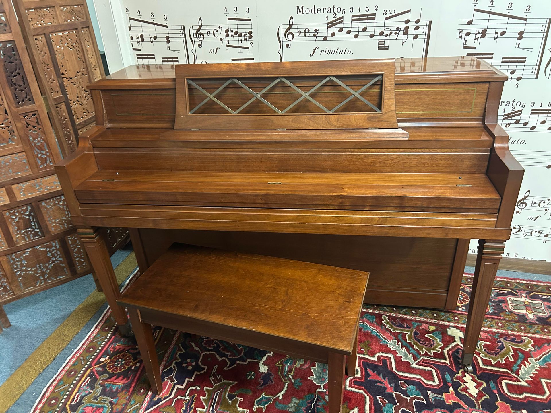 A piano with a bench in front of a wall with music notes on it.