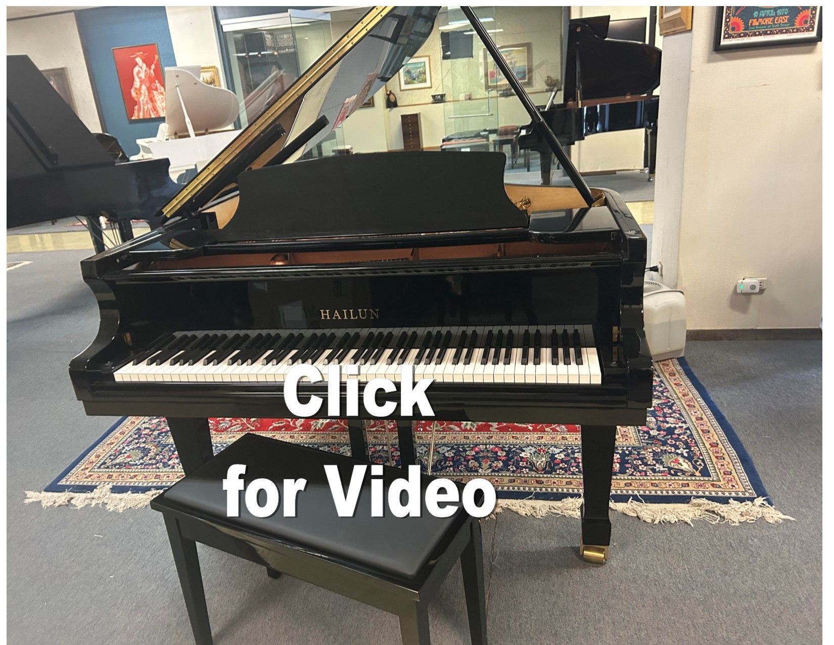A black grand piano is sitting in a room with the words click for video below it