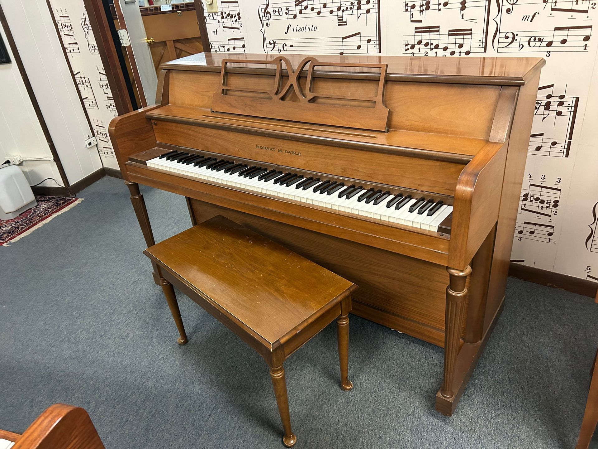 A piano with a bench next to it in a room with music notes on the wall.