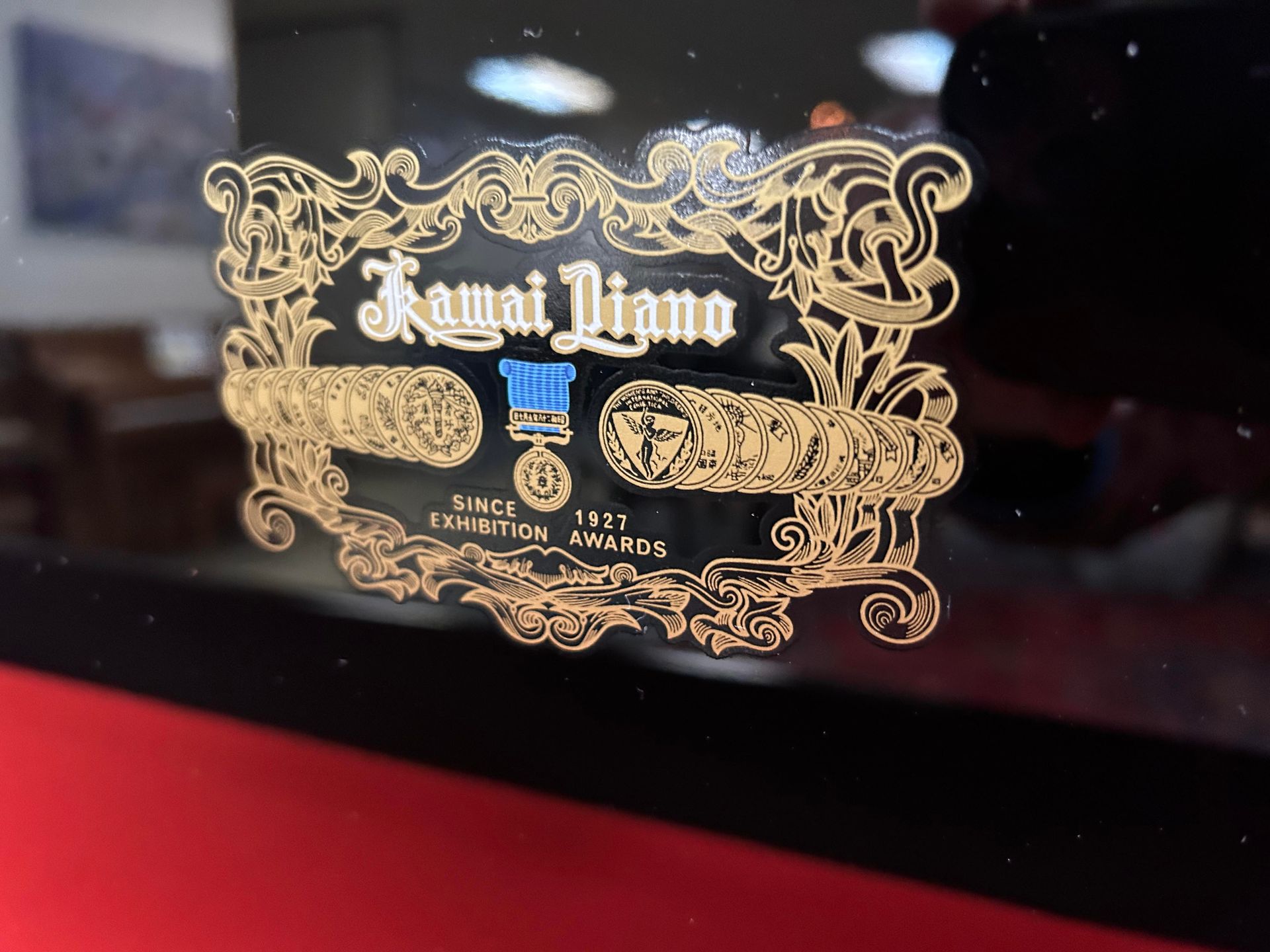 Kawai Piano logo on a piano. Gold, ornate design with text and a blue medal.