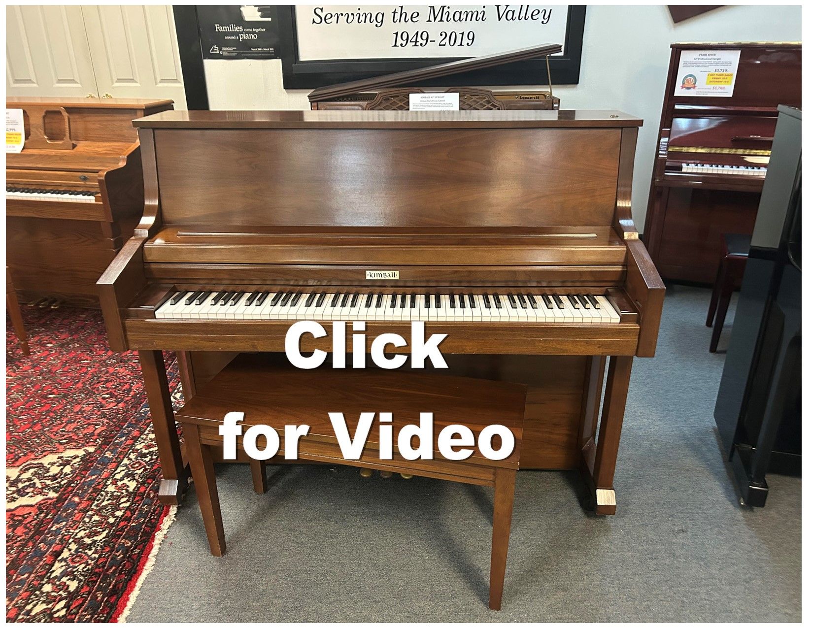 Wooden upright piano with a bench, in a store. Text overlay says