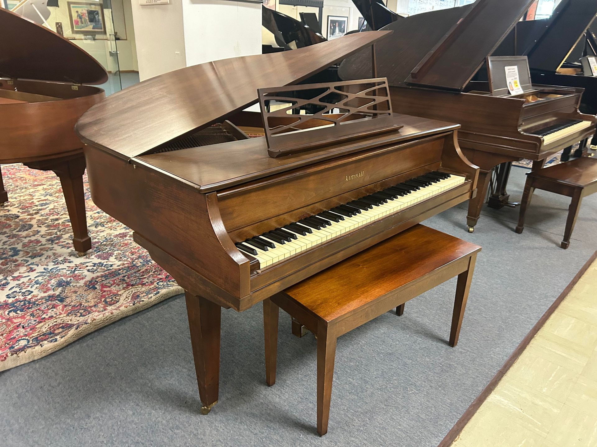 A piano with a bench underneath it is sitting in a room with other pianos.