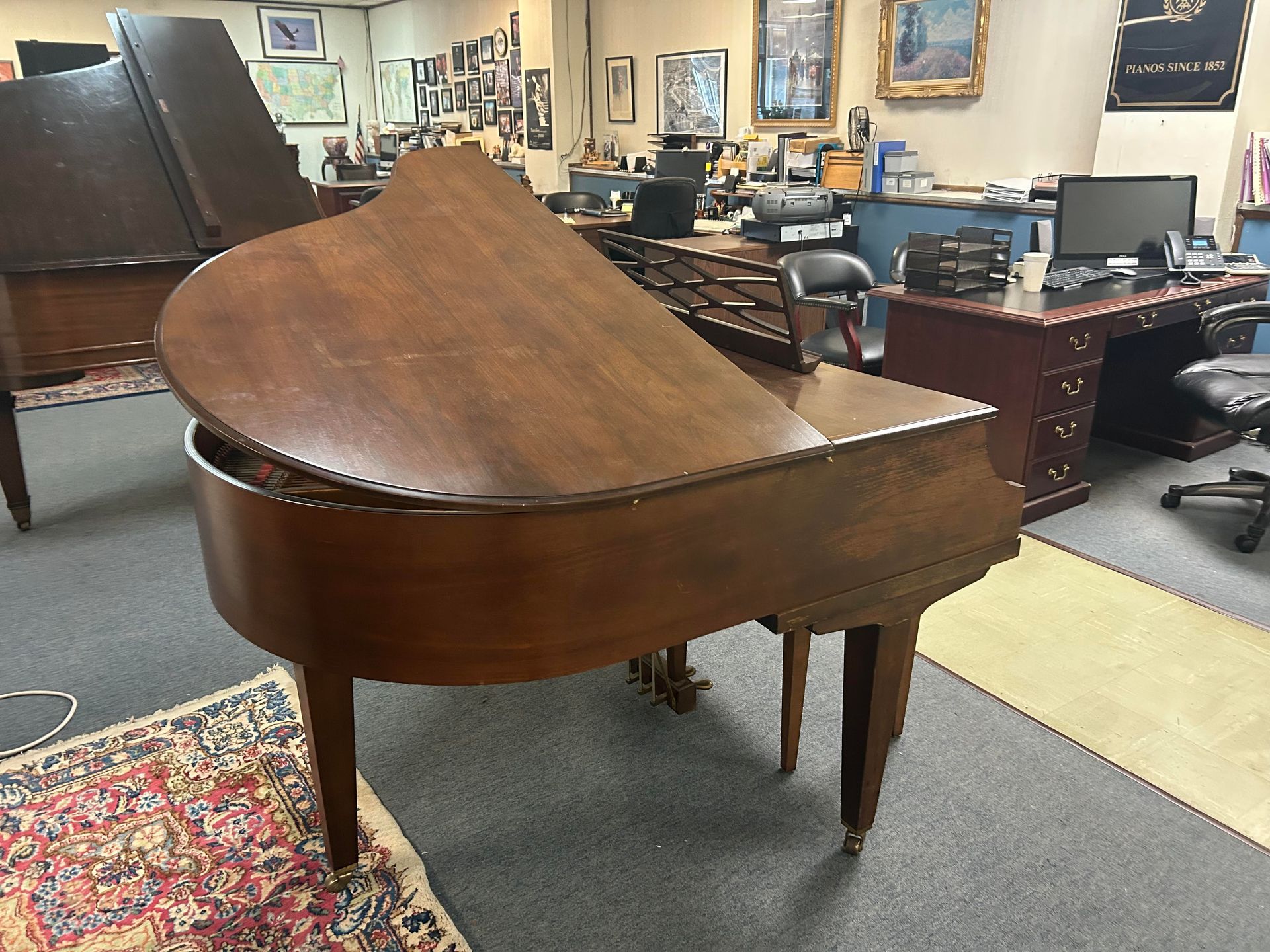 A large wooden grand piano is sitting in a room with other pianos.