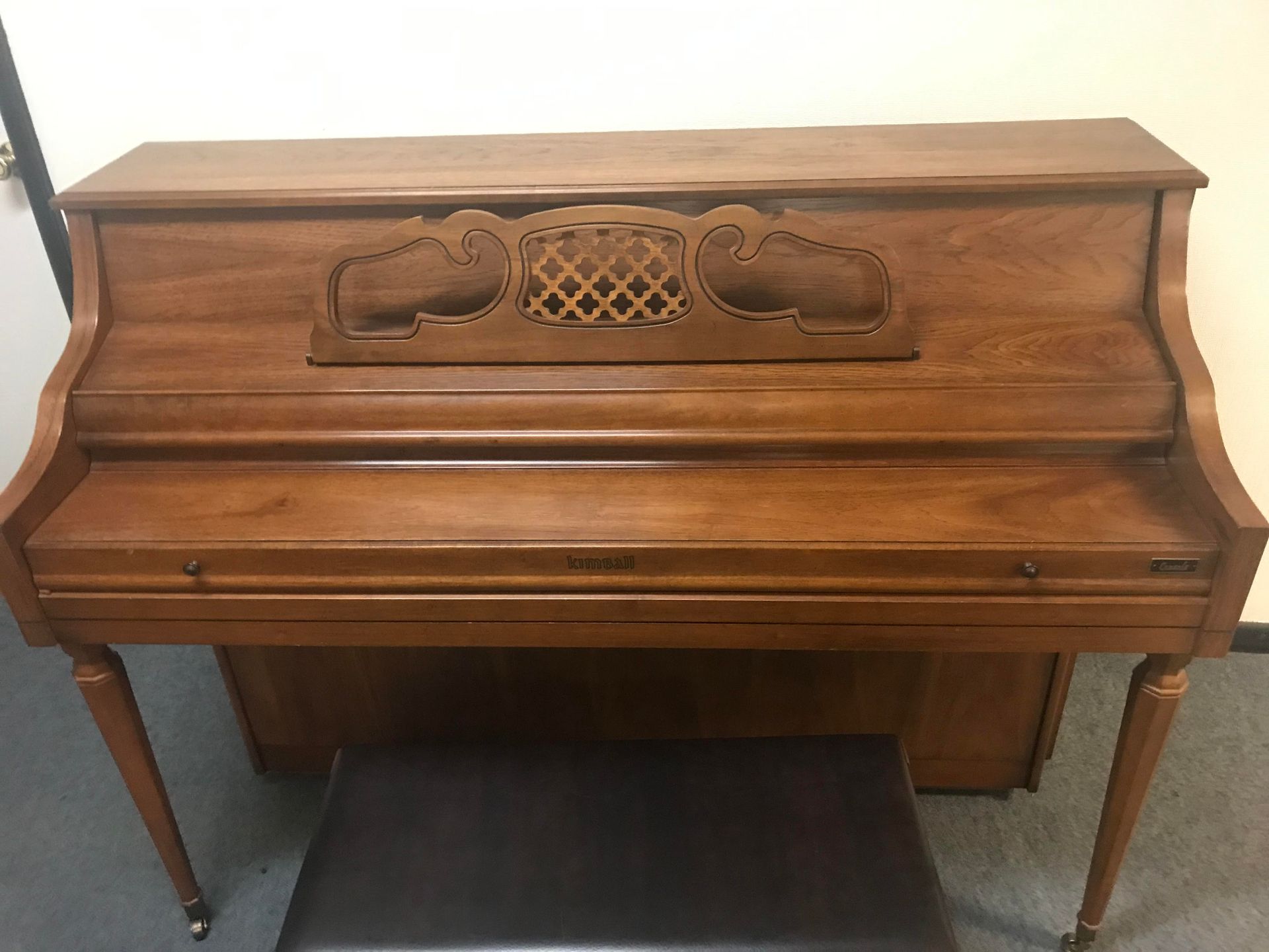 A wooden piano is sitting next to a stool in a room.