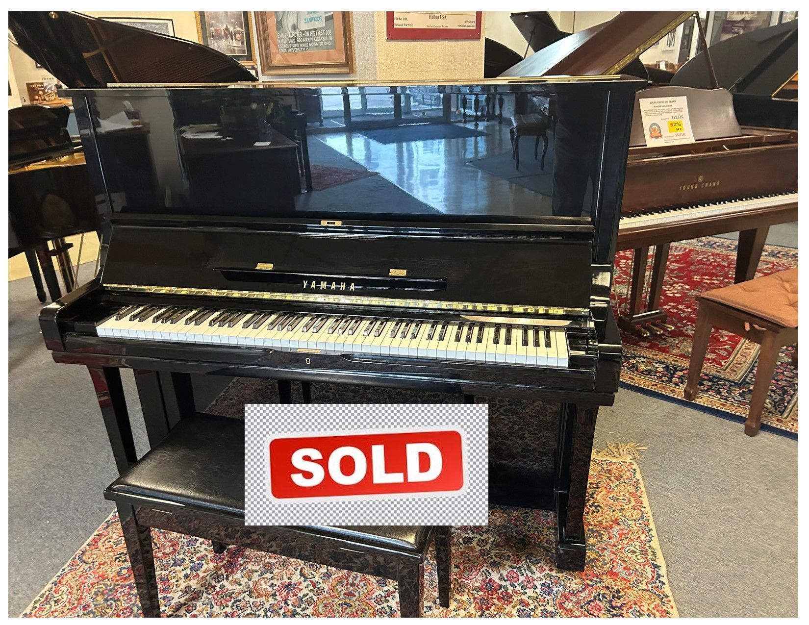 A black upright piano with a bench in a showroom, with 