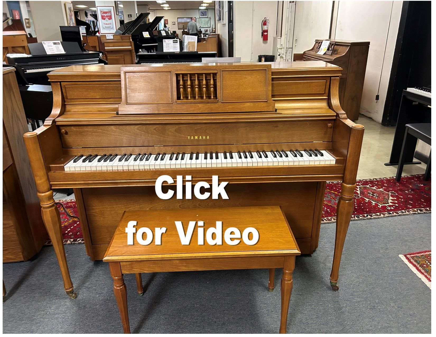 A piano is sitting on a rug with the words click for video below it.