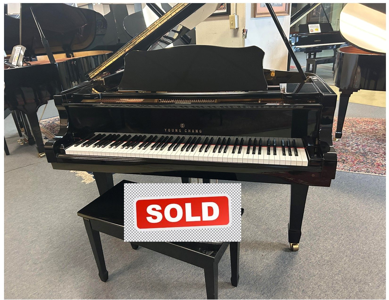 A black grand piano with a bench next to it and the words click for video below it