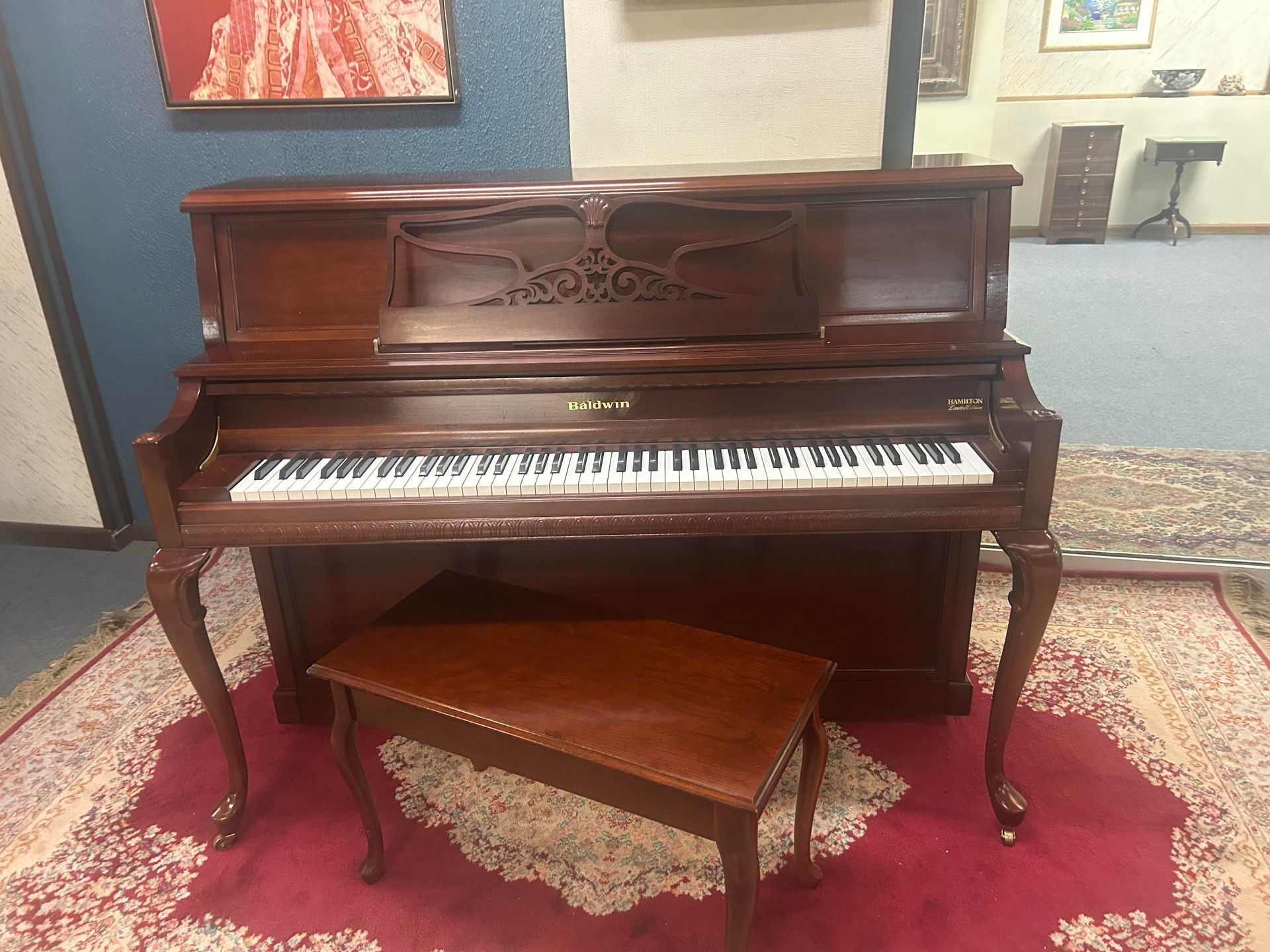 Mahogany upright piano with bench on a red rug in a room.