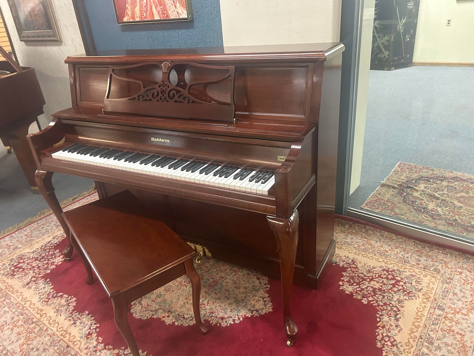 Brown upright piano with matching bench on a patterned rug.