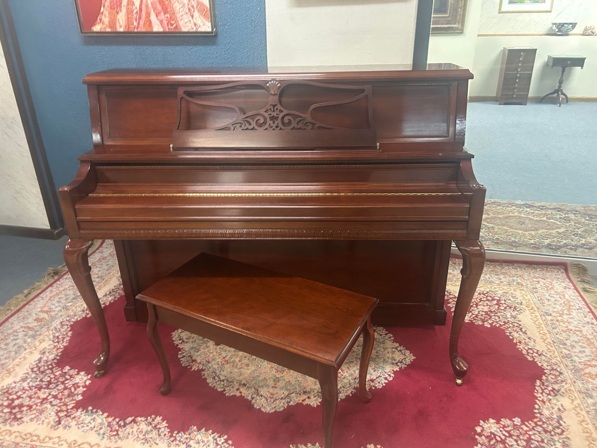A dark brown upright piano with a matching bench on a red rug.