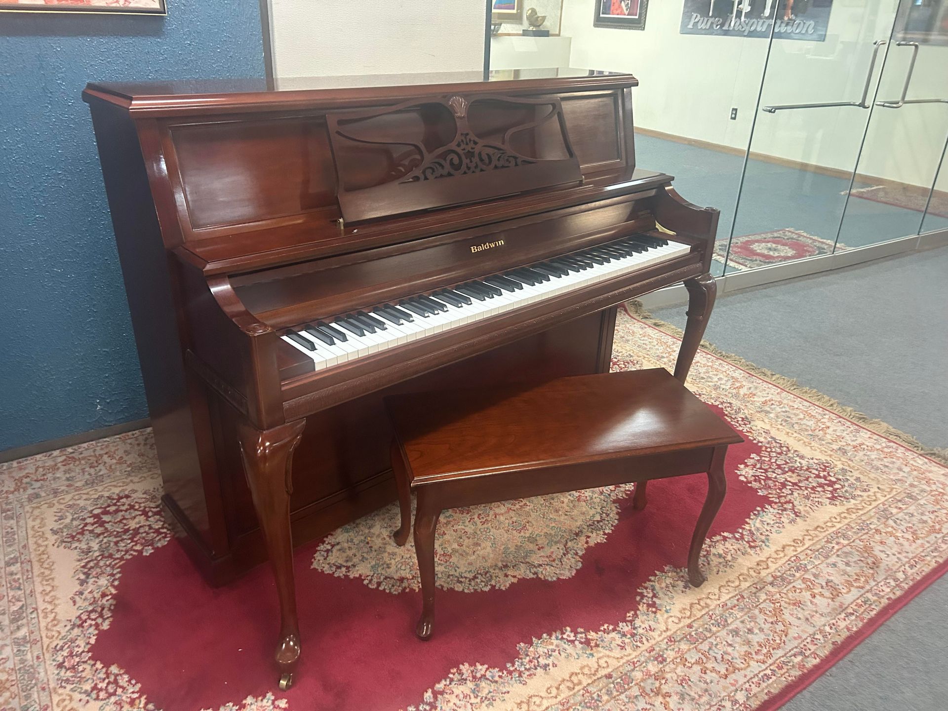 Brown upright piano with matching bench on a red rug.