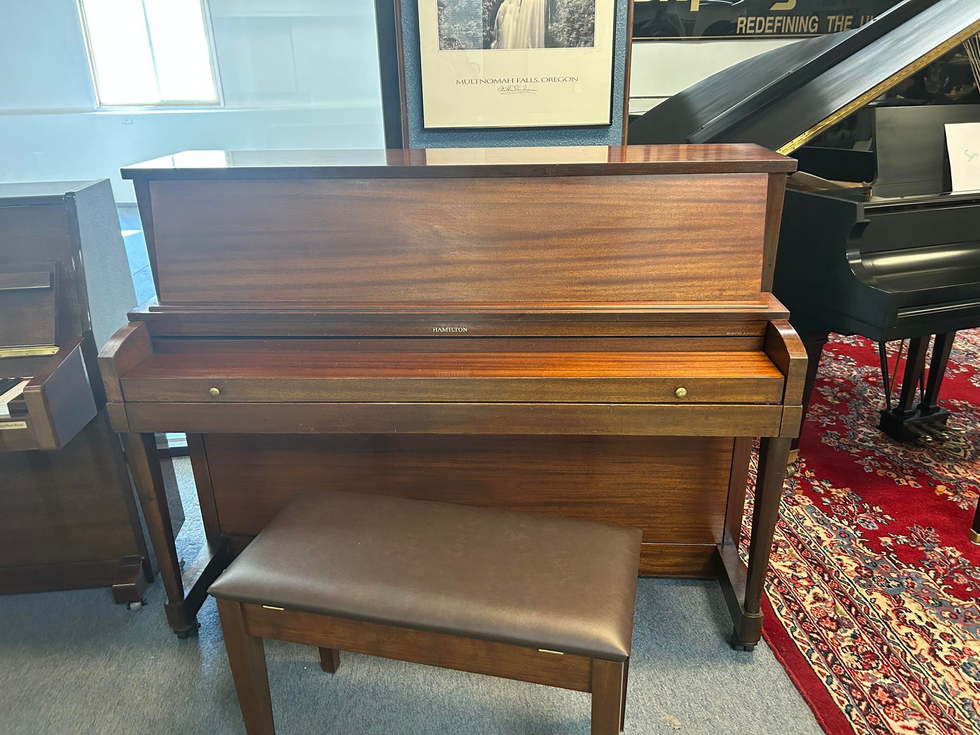 Wooden upright piano with bench in a room with other pianos.
