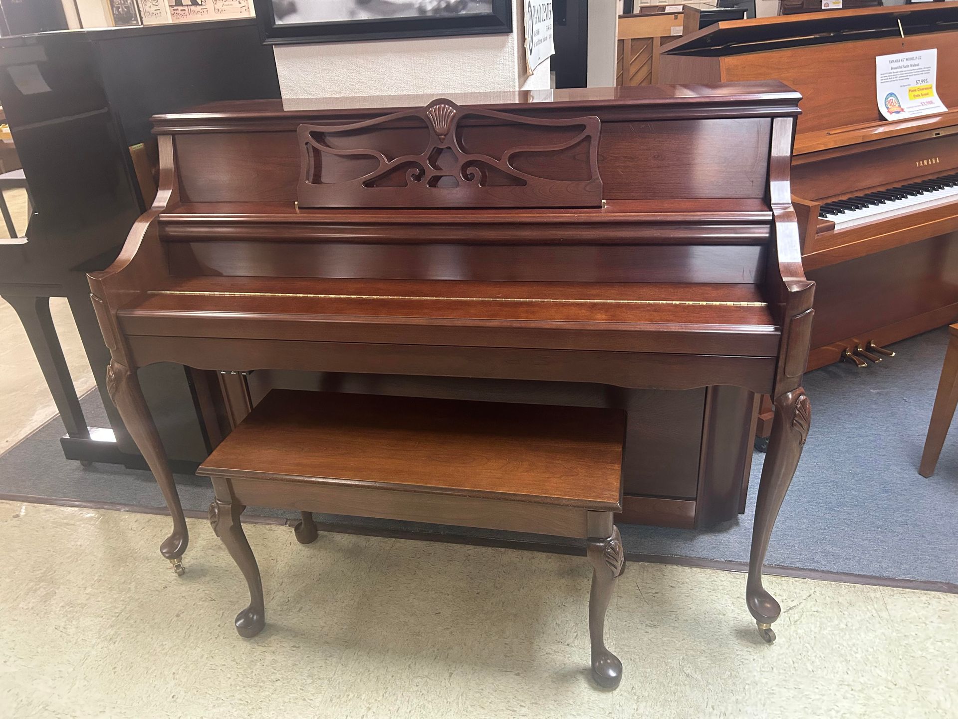 Brown upright piano with a matching bench in a furniture store.