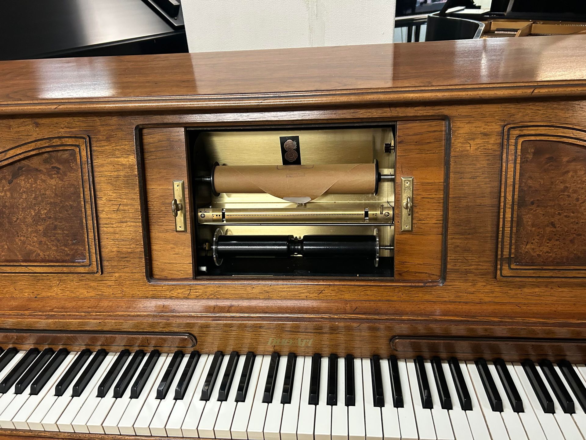 A wooden player piano with a roll visible in the center. The keyboard is below.