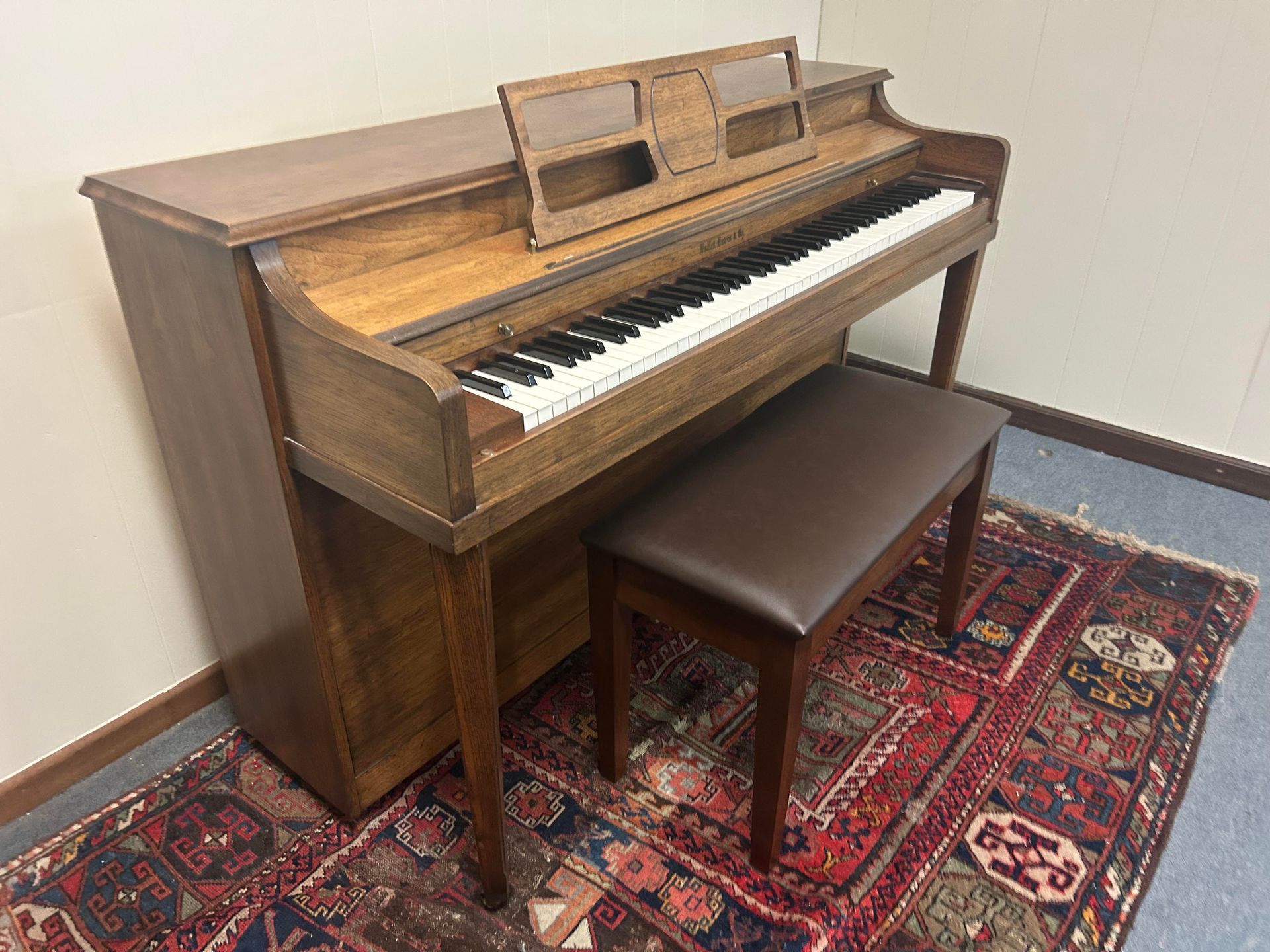 Wooden upright piano with bench on a patterned rug.