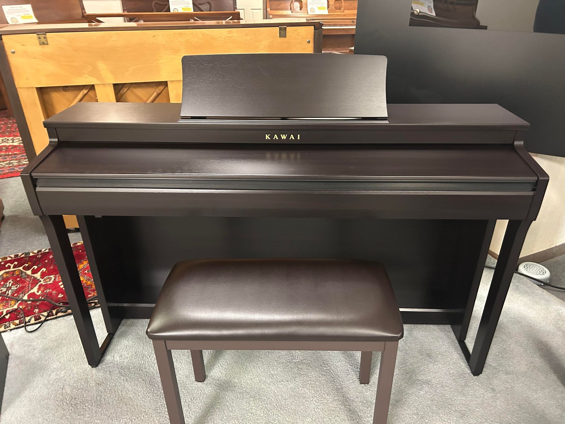 Dark brown Kawai digital piano with music rest and matching bench in a room.