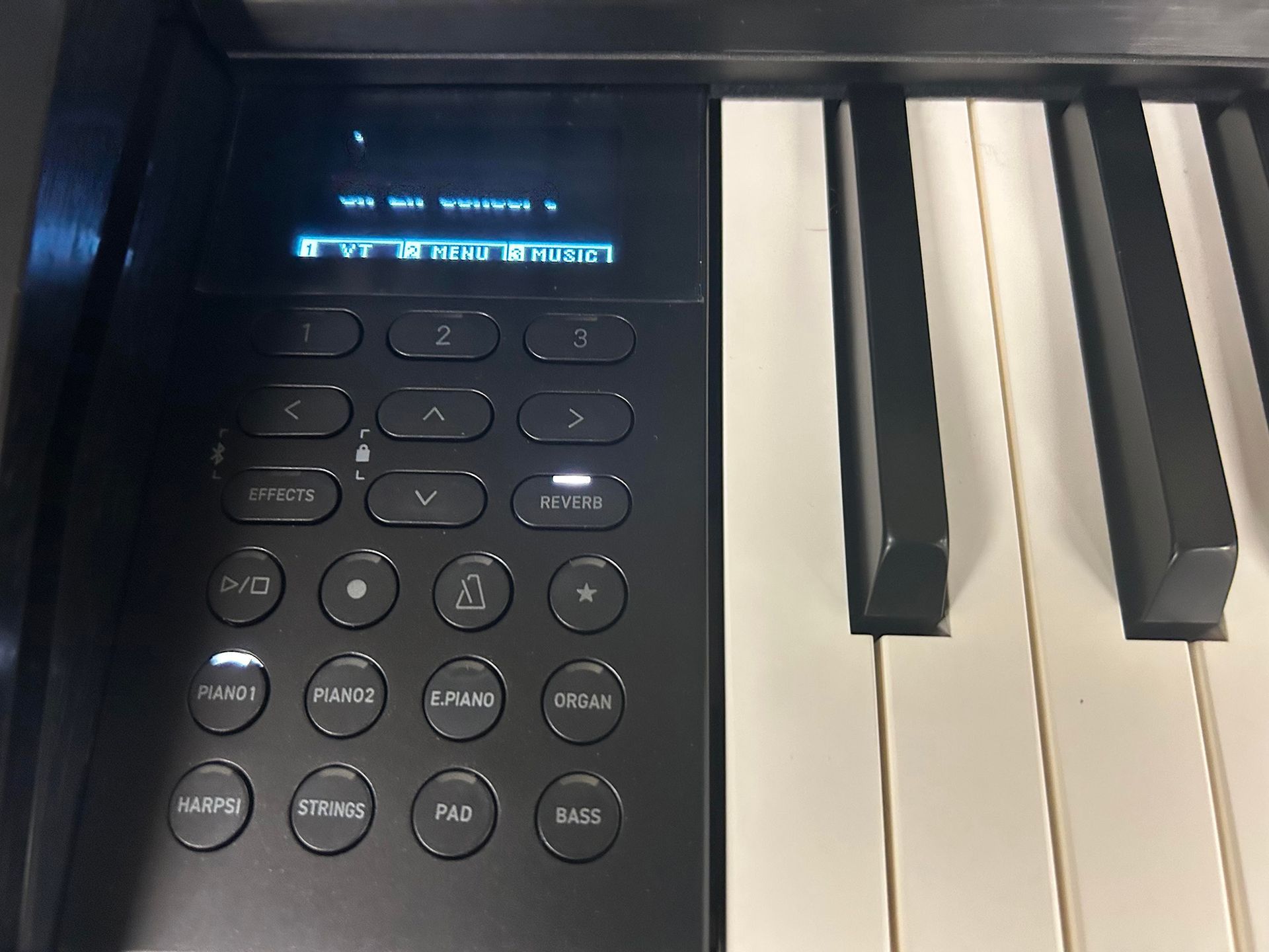 Black digital piano's control panel with an illuminated screen and buttons next to white and black keys.