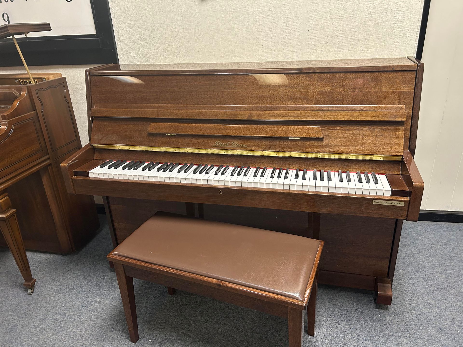 11351 - Pearl River 43, Upright piano with bench; wood finish, keys exposed, slight damage to the top, indoors.