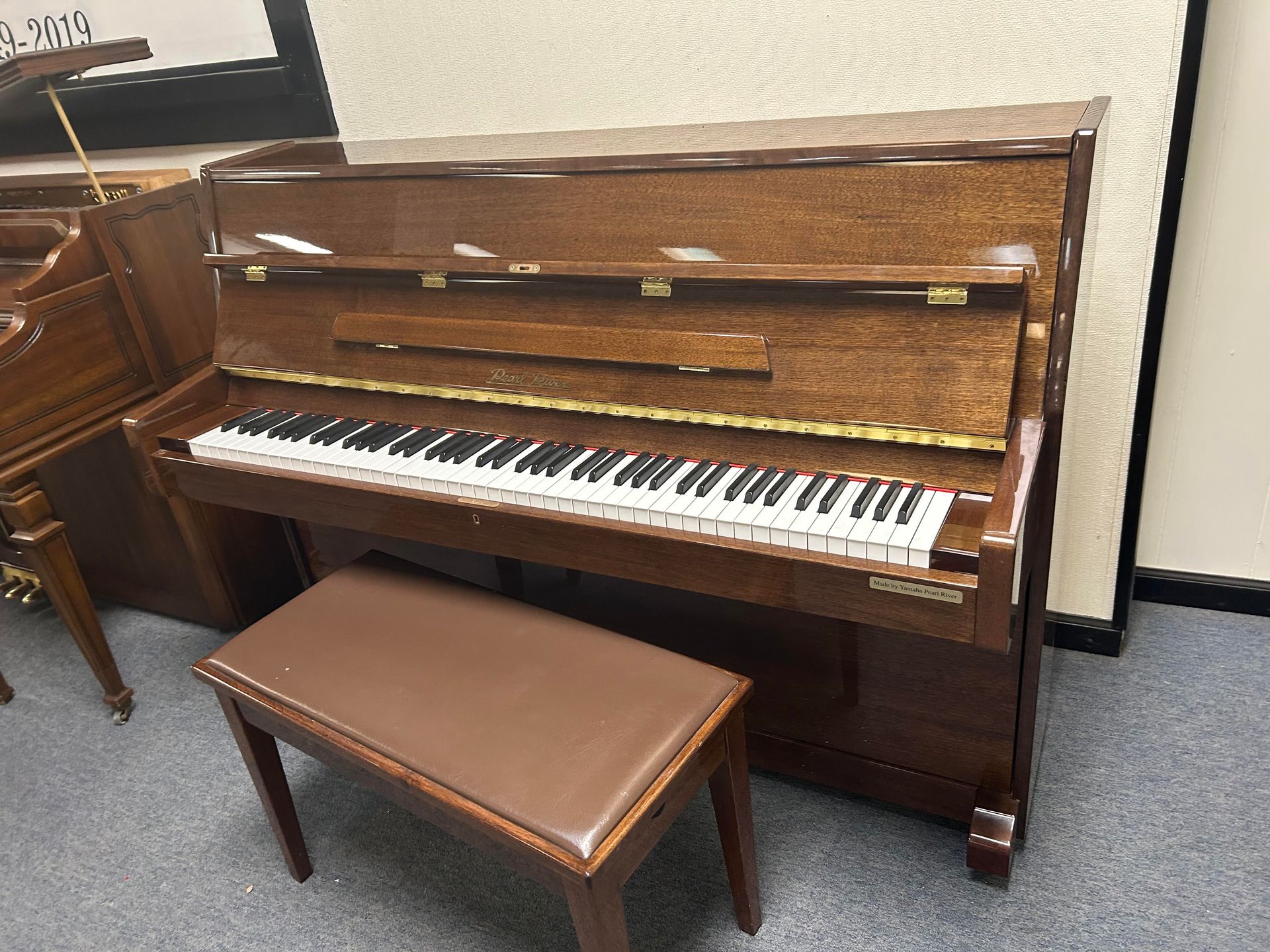 11351 - Pearl River 43, Wooden upright piano with bench; brown tones, keys visible.