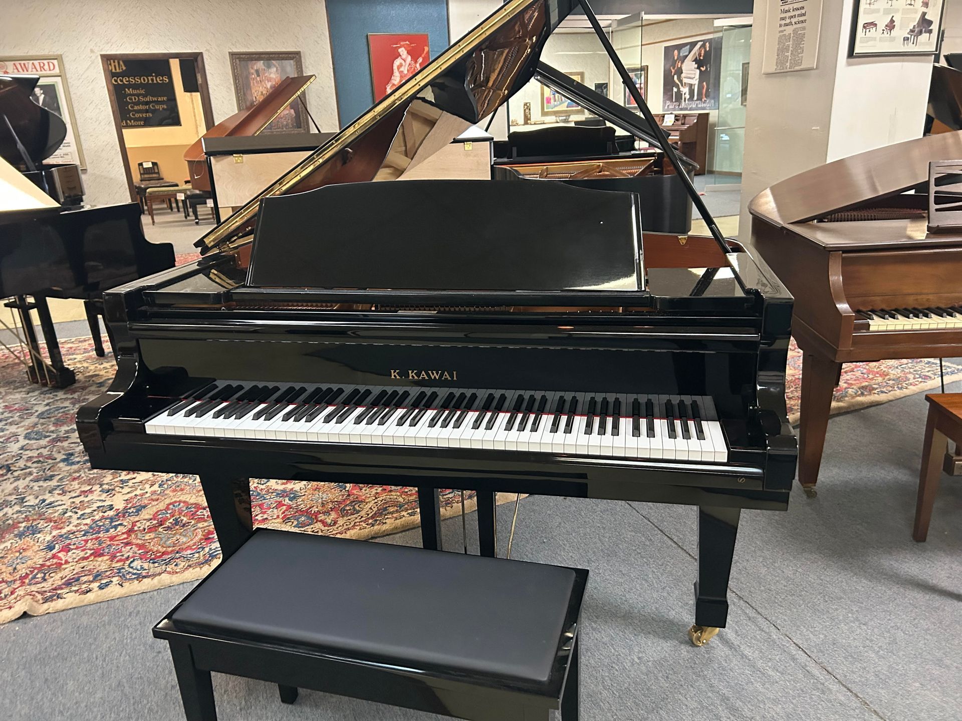 Black grand piano with open lid, set in a showroom with other pianos. Bench in front.