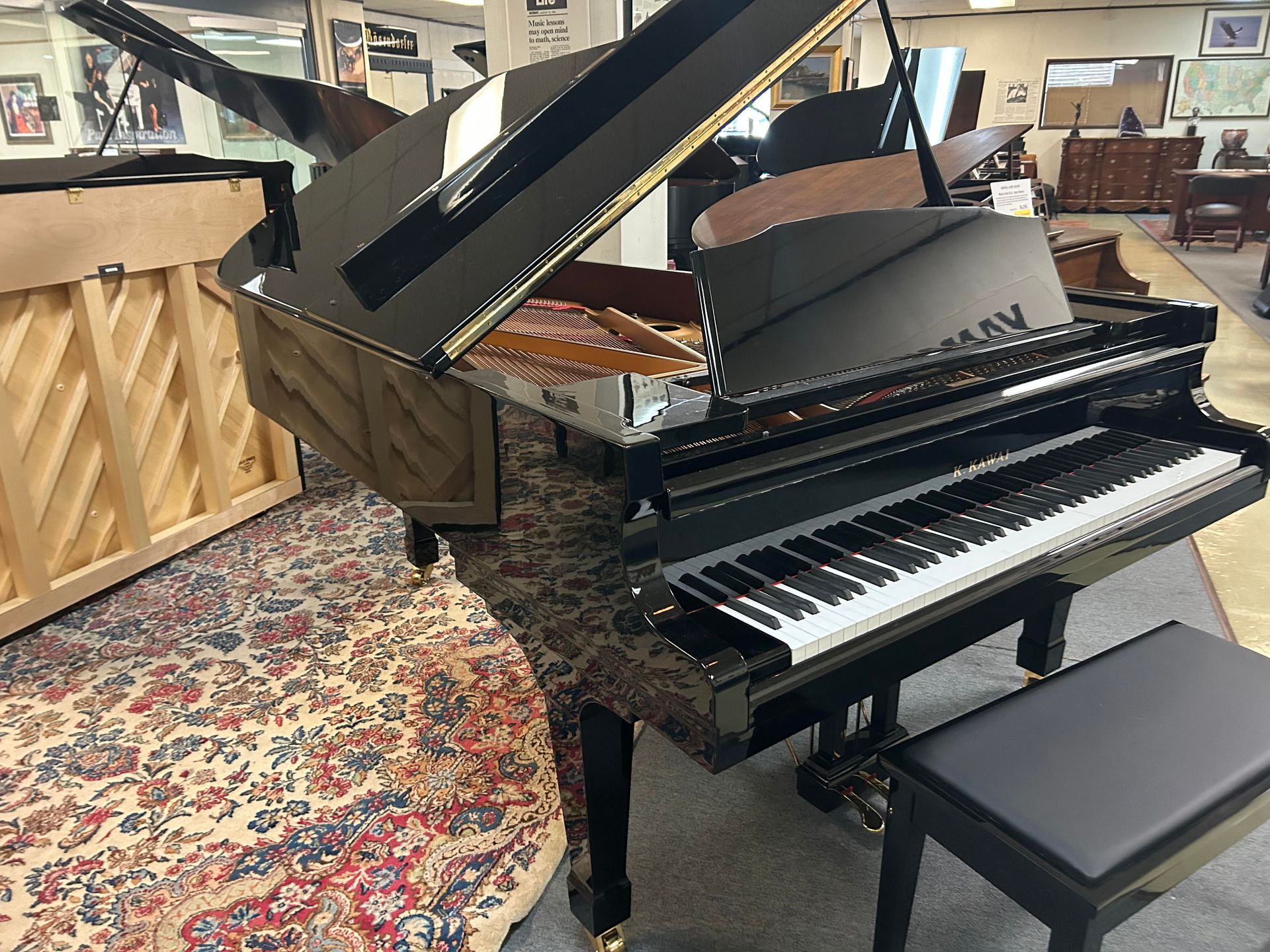 Black grand piano with open lid, keyboard and bench, in a showroom setting.
