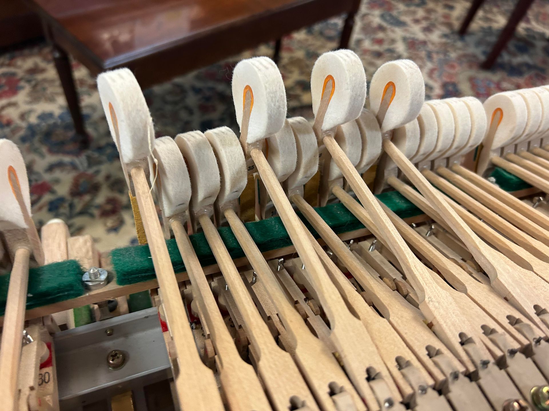 A close up of the inside of a piano with a bench in the background.