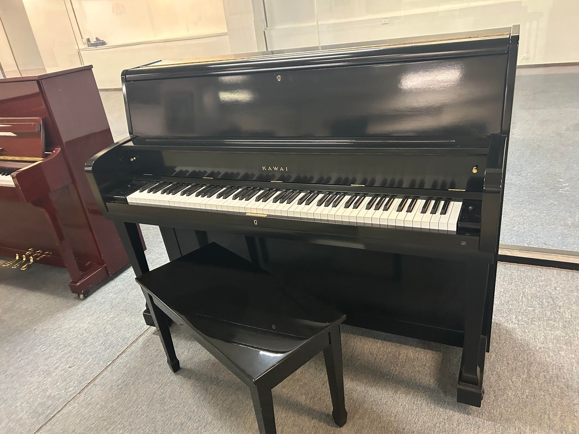 Black upright piano with matching bench in a room with a red piano.